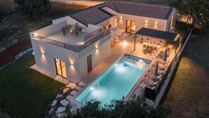 A modern house with a swimming pool, outdoor seating, and a well-lit patio area.
