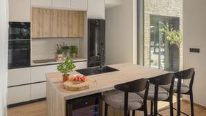 A modern kitchen with a central island, bar stools, and a view of a stone building outside. - Luxury Villa in Tar With View (Tar-Vabriga)
