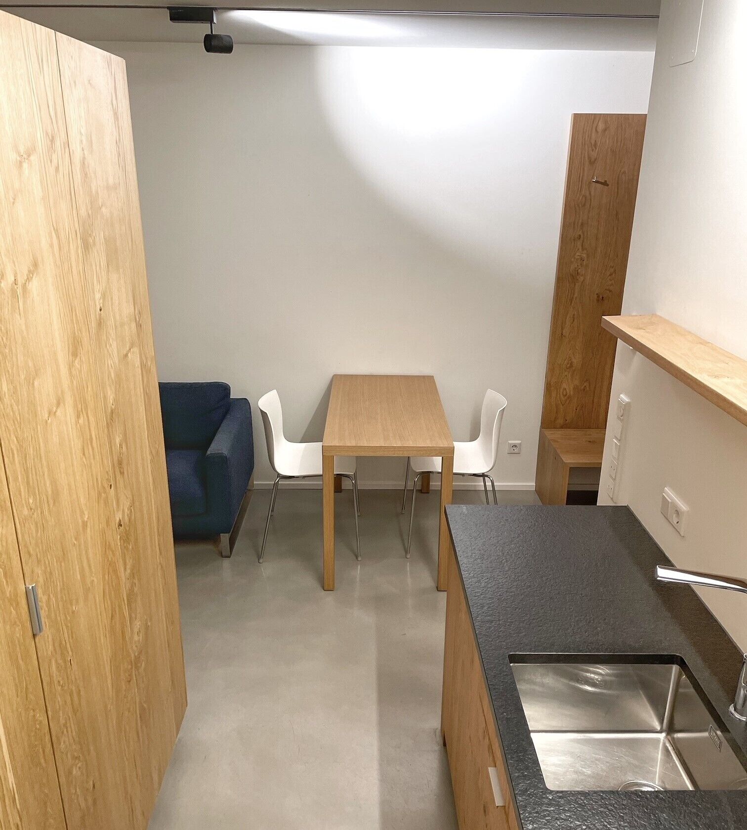 A compact kitchen with a wooden table, white chairs, and a built-in sink.