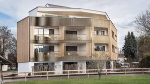 A modern multi-story building with a flat roof, wooden slatted balconies, and a white facade. - Apartmenthaus Anna - Self-Check-in (Lustenau)