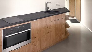 A modern kitchen with wooden cabinets, a black countertop, a built-in oven, and a stainless steel sink. - Apartmenthaus Anna - Self-Check-in (Lustenau)