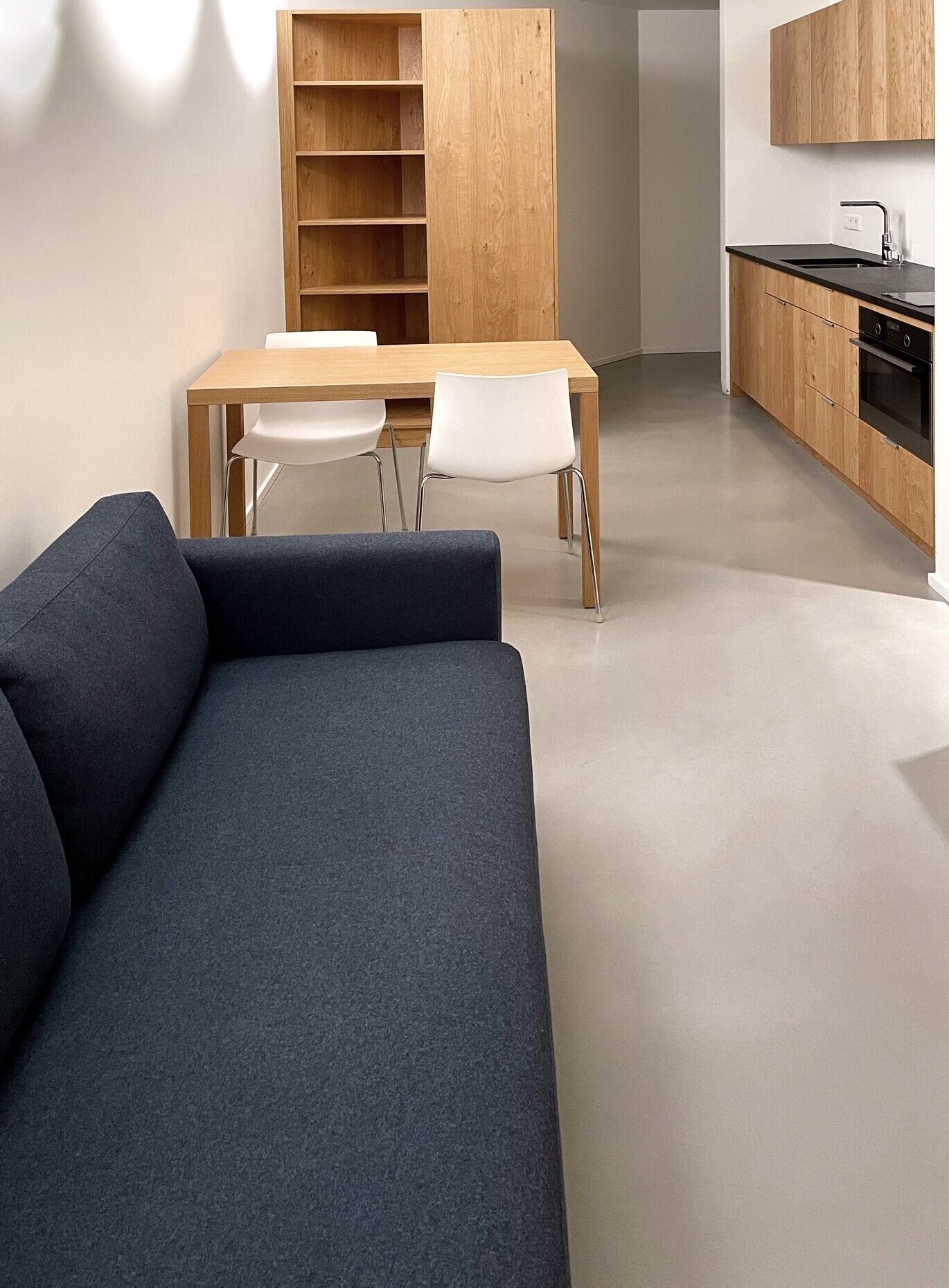 A modern kitchen with a wooden table and chairs, a built-in oven, and a black countertop.