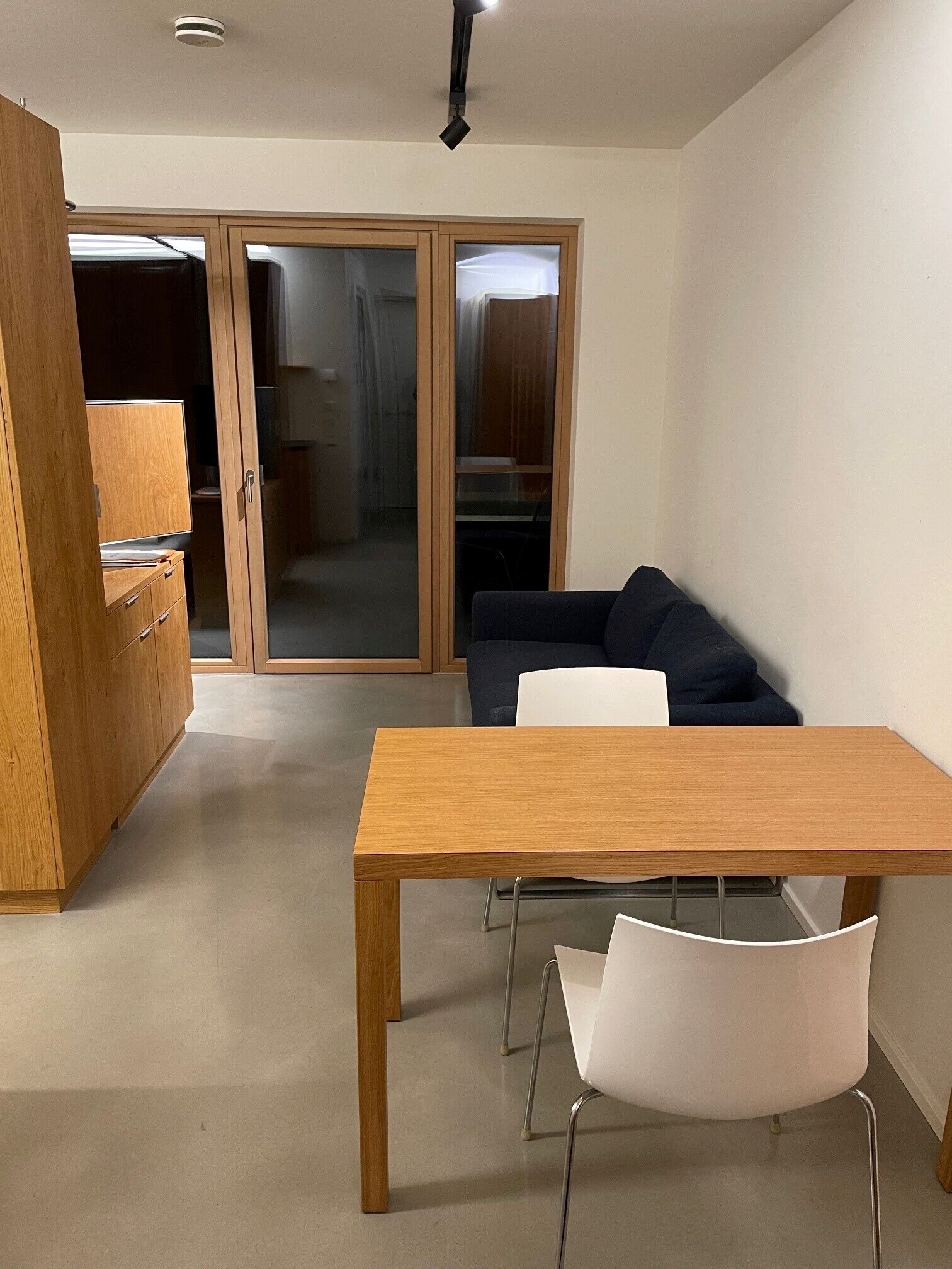 Una sala moderna con una mesa de comedor de madera, sillas blancas, un sofá azul oscuro y un divisor deslizante de vidrio que da a una zona de cocina.