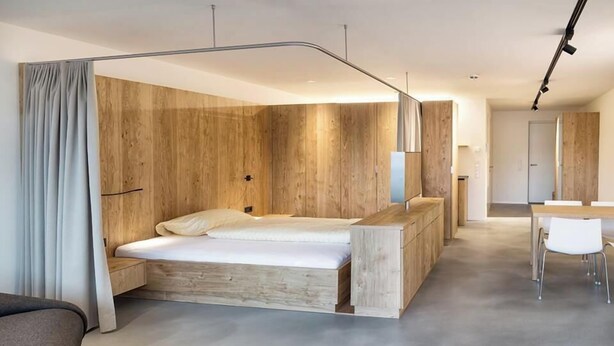 A modern bedroom with a wooden headboard, a large bed, a desk, and a chair. - Apartmenthaus Anna - Self-Check-in (Lustenau)