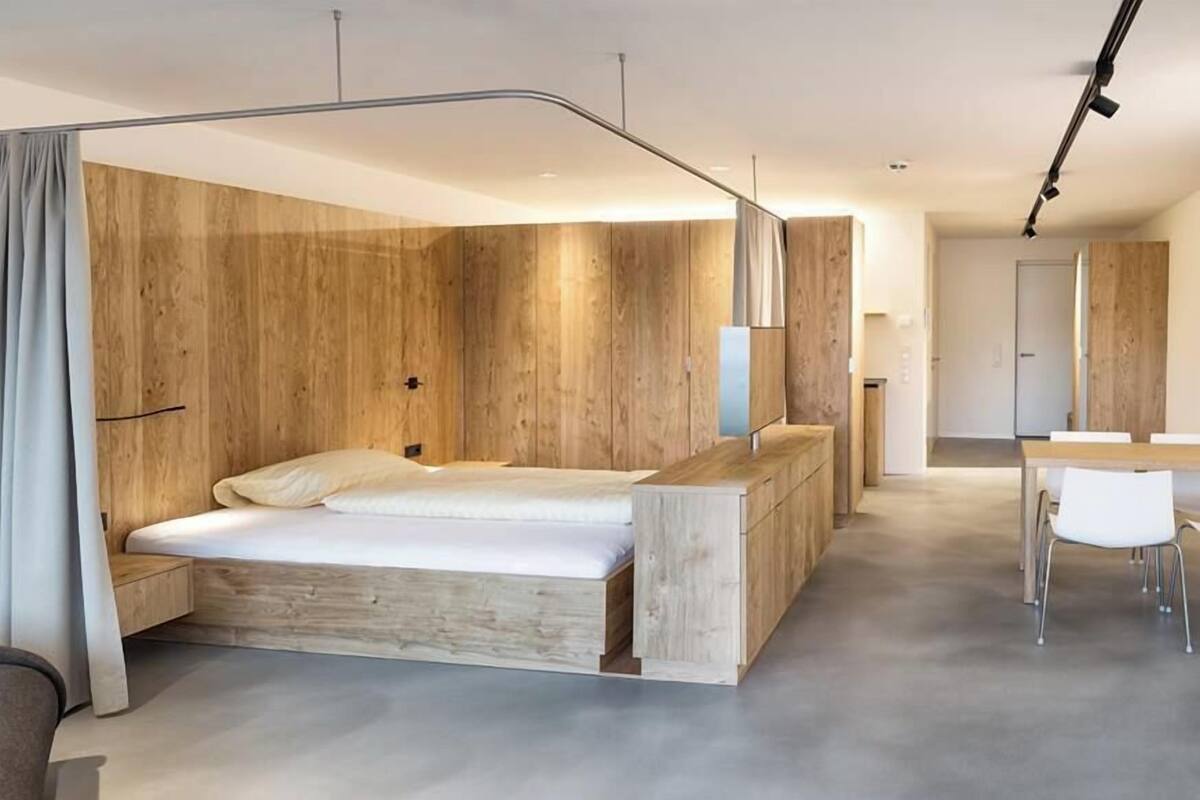 A modern bedroom with a wooden headboard, a large bed, a desk, and a chair.