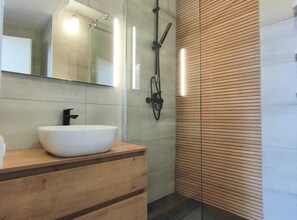 Ein modernes Badezimmer mit einem großen, weißen Waschbecken, einem Spiegel und einer Dusche inklusive Handbrause.