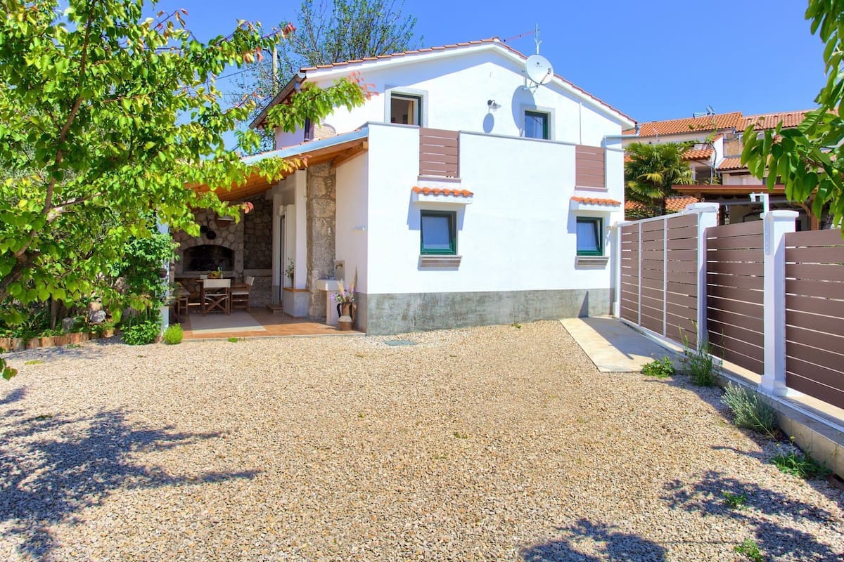 Une maison à deux étages avec une cheminée en pierre, un patio couvert et une allée en gravier.