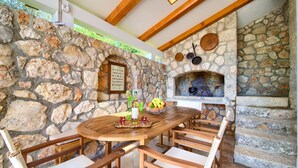 A stone-walled outdoor dining area with a round wooden table and chairs, a stone fireplace, and a view of the sky through a skylight. - Tranquil Getaway Polje Villa With Pool (Dobrinj)