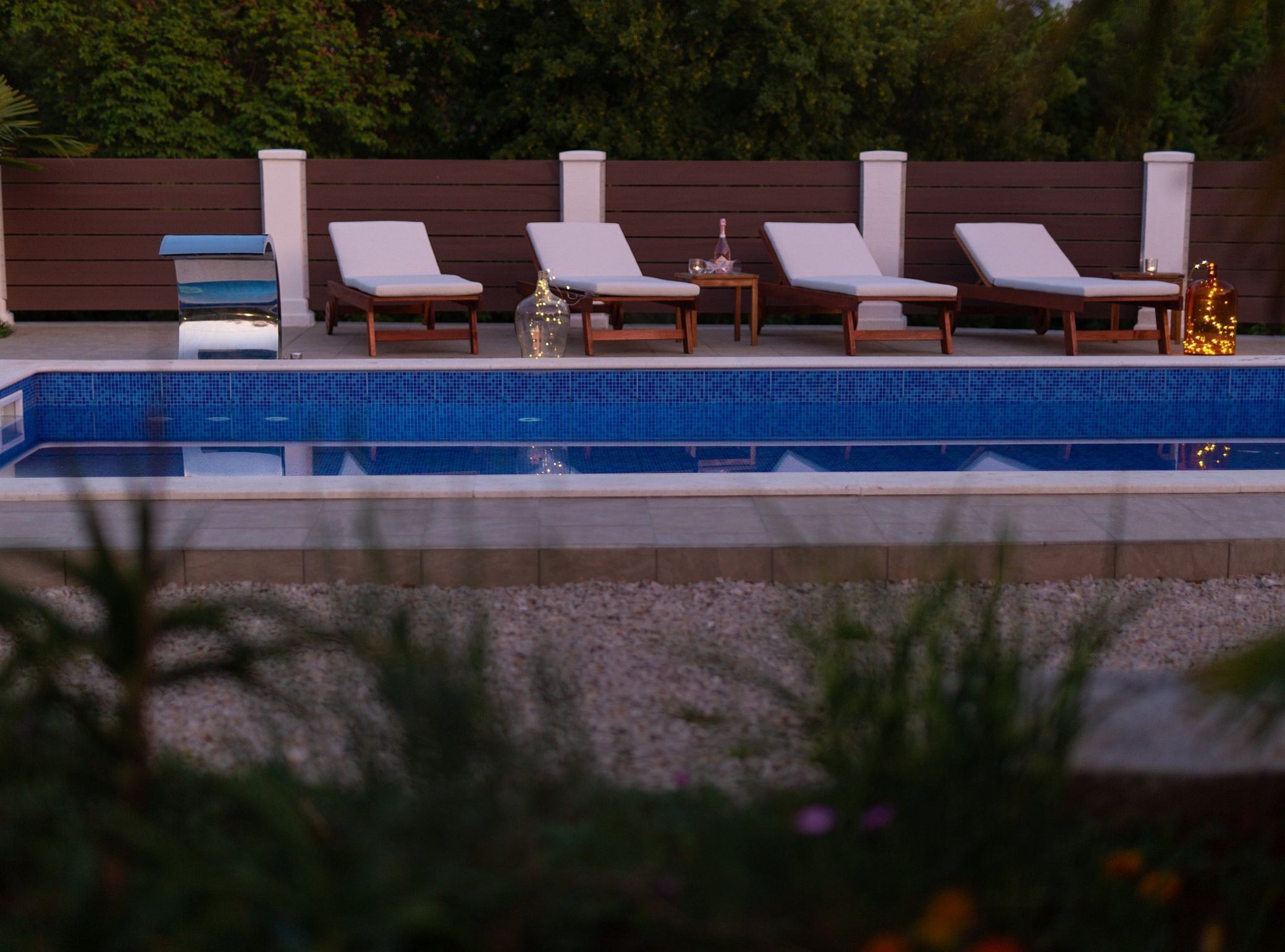 Una piscina con sillas de descanso y una pequeña mesa con una botella y un vaso.