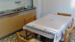 A small kitchen with a sink, a table with a tablecloth, and wooden chairs. - Airy Crikvenica Apartment With Terrace Close to Beach (Crikvenica)