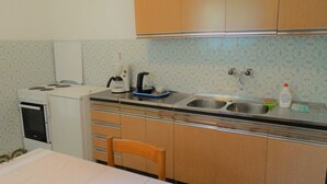 A compact kitchen with a stove, coffee maker, sink, and wooden cabinets. - Airy Crikvenica Apartment With Terrace Close to Beach (Crikvenica)