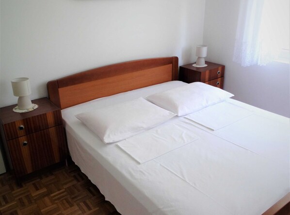 Un letto ben rifatto con lenzuola bianche, una testiera in legno e due comodini con lampade.