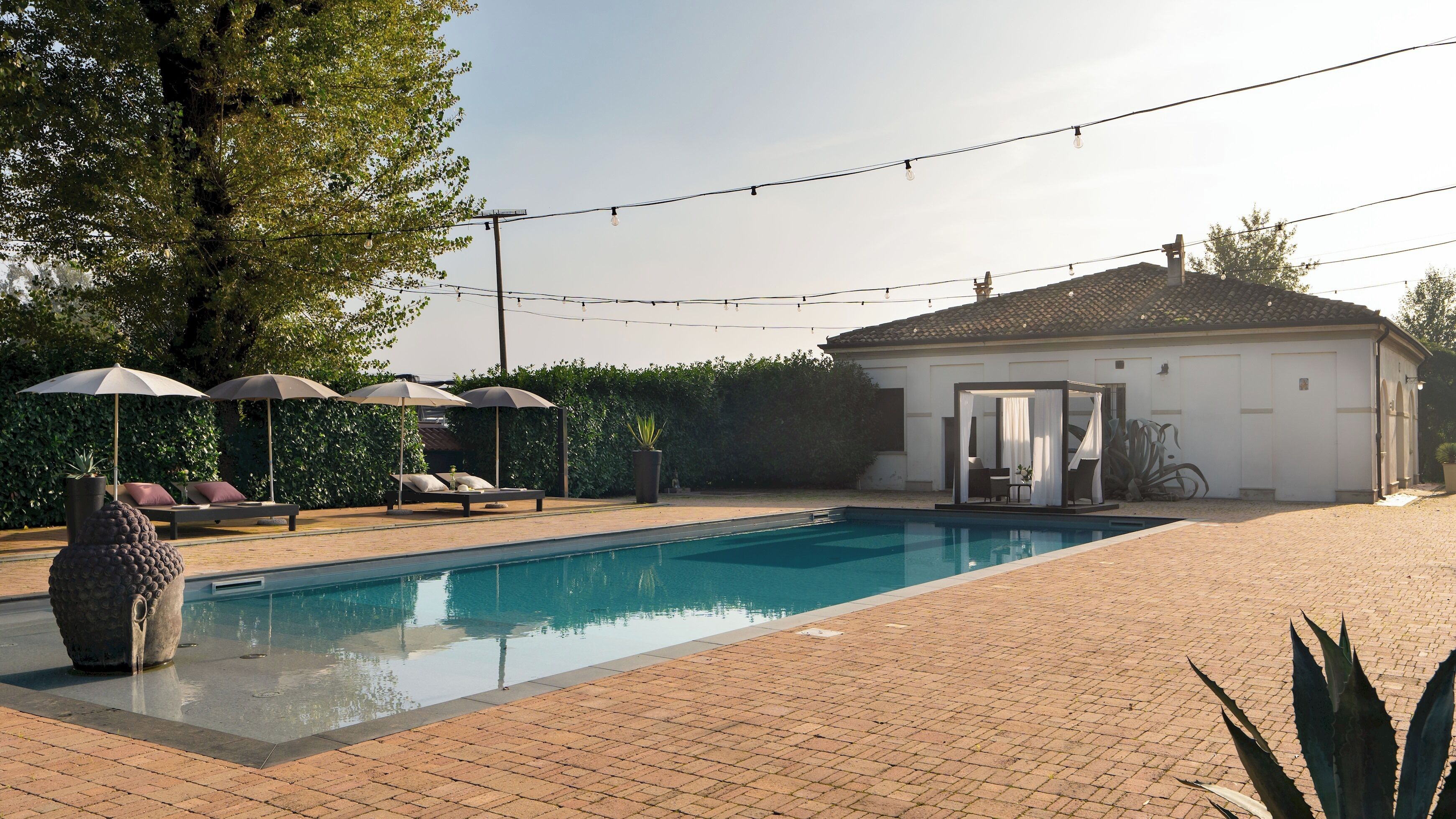 Una piscina con lettini e ombrelloni, una zona relax coperta e un edificio con tetto in tegole.