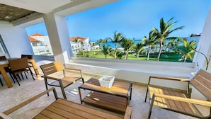 A balcony with wooden furniture and a view of palm trees and buildings. - Apt With 2BR and Beach Access in Punta Palmera (Punta Cana)
