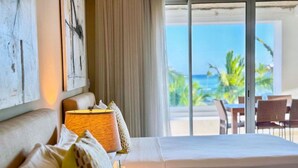 A hotel room with a large bed, a lamp, and a view of the ocean. - Apt With 2BR and Beach Access in Punta Palmera (Punta Cana)