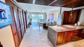 A spacious kitchen with a granite countertop and wooden cabinets, a dining area with a table and chairs, and a view of the outdoors through large windows. - Apt With 2BR and Beach Access in Punta Palmera (Punta Cana)