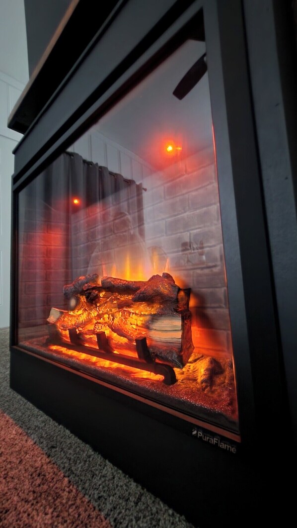 A glass-fronted fireplace with burning logs, a visible brick wall, and a red light above the fire.
