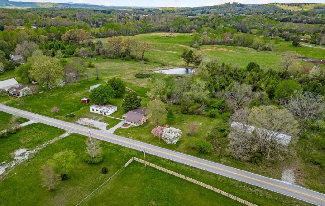 An aerial view of a rural property with a main house, a pond, and surrounding greenery.