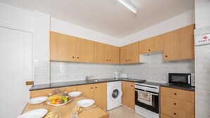 A modern kitchen with wooden cabinets, a washing machine, a stove, and a microwave. - GE Harbour Apartments 16 (Polis)