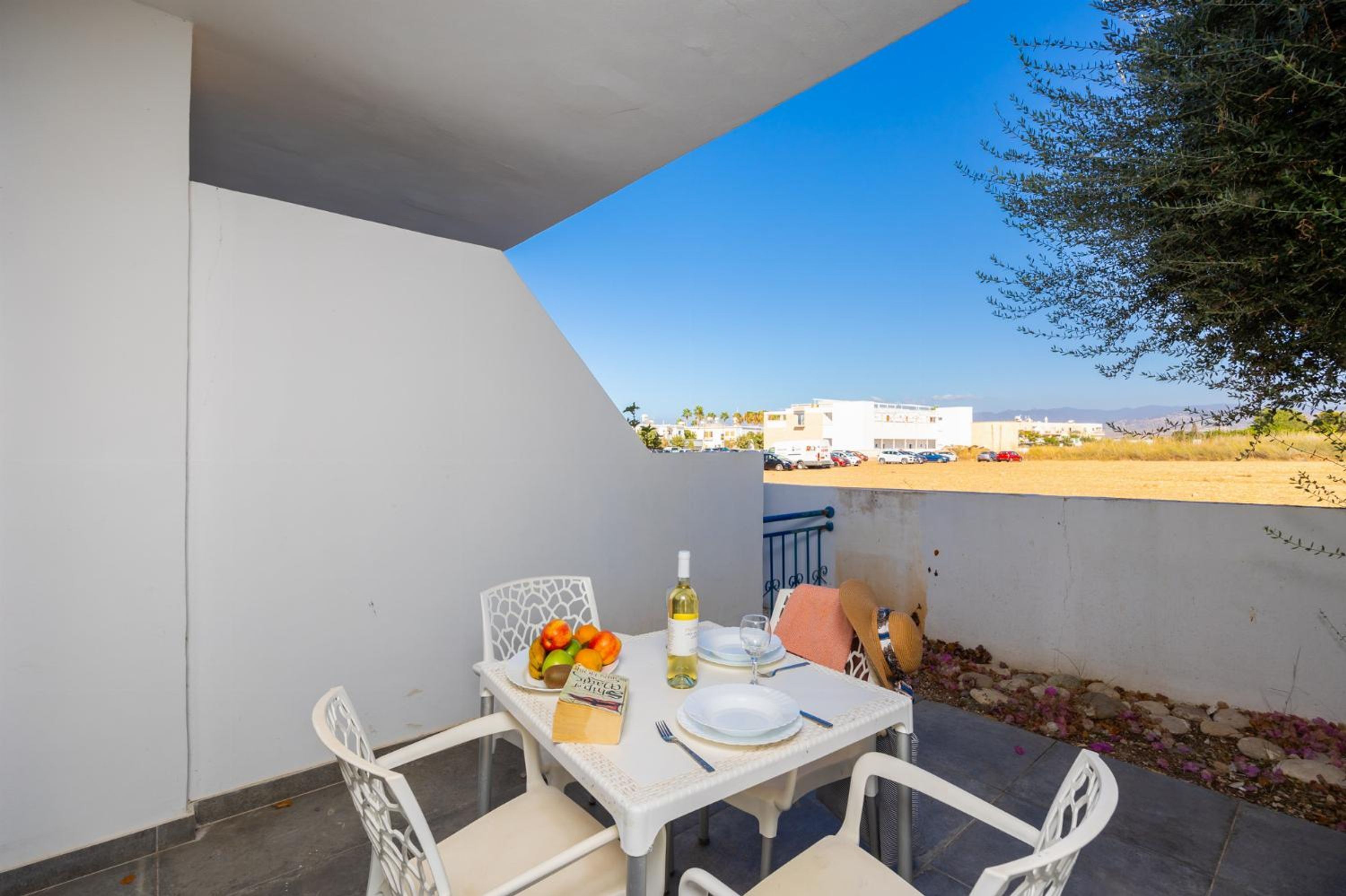 A balcony with a table set for two, featuring a bottle of white wine, a plate of fruit, and a menu.