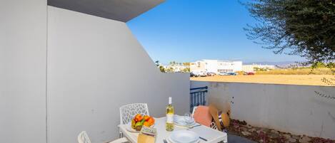 A balcony with a table set for two, featuring a bottle of white wine, a plate of fruit, and a menu.