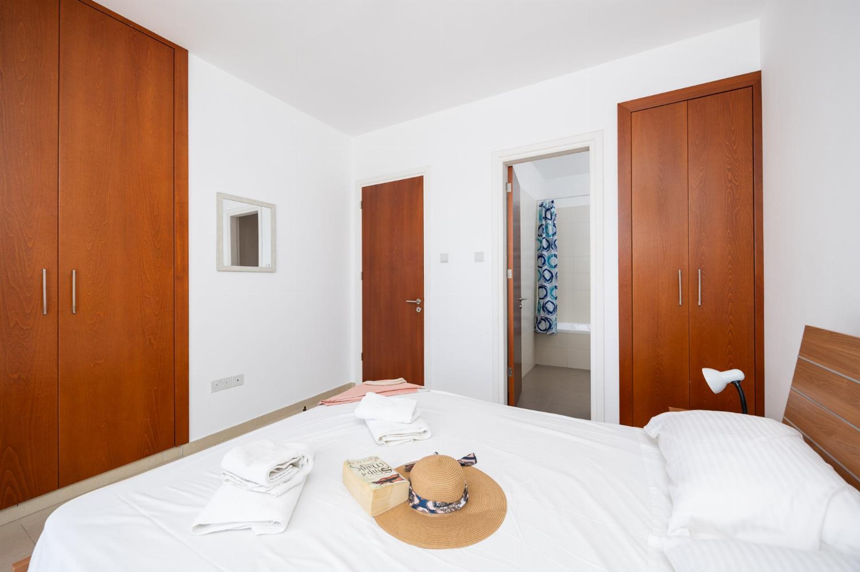 Quarto com cama, guarda-roupa de madeira, espelho e porta de banheiro.
