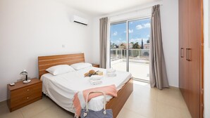 Ein modernes Hotelzimmer mit einem großen Bett, einem Nachttisch mit Lampe, einem Kleiderschrank und einem Balkon mit Vorhängen.