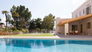 A swimming pool with a stone wall and a patio area with outdoor furniture. - Villa Nafsika in Vamos (Apokoronas)
