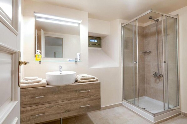 A modern bathroom with a wooden vanity, a large mirror, a glass-enclosed shower, and a small window. - Villa Nafsika in Vamos (Apokoronas)