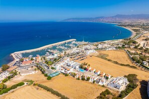 An aerial view of a coastal town with a marina, residential buildings, and a large sandy area. - GE Harbour Maisonette (Polis)