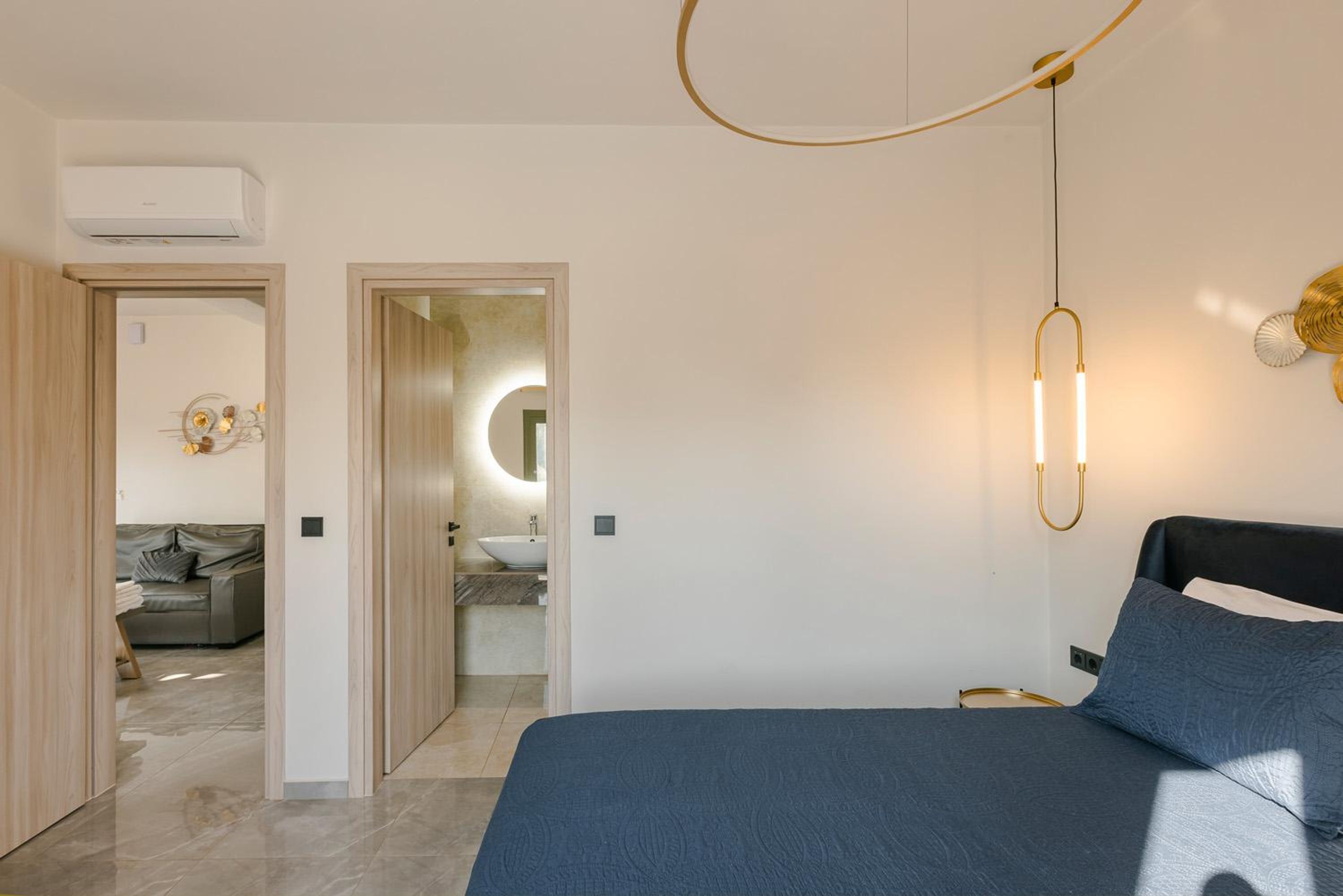 Ein modernes Schlafzimmer mit einem großen Bett, einem Nachttisch, einer Wandleuchte und Blick ins Badezimmer.