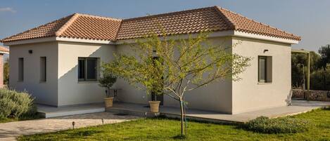 A modern two-story house with a tiled roof, a small front yard with a tree, and a pathway leading to the entrance.