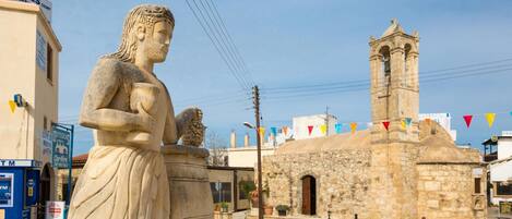 A stone statue in a square with a church tower in the background.