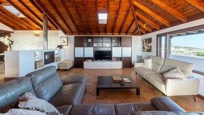 A spacious living area with a high wooden ceiling, a flat-screen TV, and a large window offering a view of the outdoors. - Villa Asomada in La Asomada (Tías)
