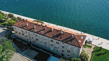An aerial view of a multi-story building with a red-tiled roof, adjacent to a waterfront promenade.