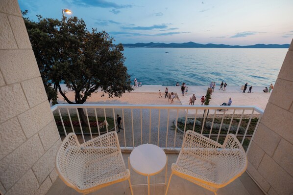 A balcony with wicker chairs and a small table, overlooking a beach with people and a tree. - Mona Lisa's view in Zadar Old Town (Zadar)