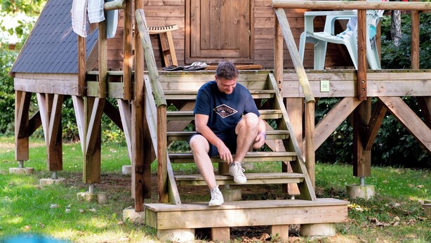 A wooden cabin with a porch, a set of stairs, and a small table. - Camping de Thoissey - Val de Saône (Saint-Didier-sur-Chalaronne)