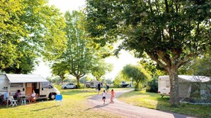 A campsite with RVs parked on a dirt path, surrounded by trees and grass. - Camping de Thoissey - Val de Saône (Saint-Didier-sur-Chalaronne)