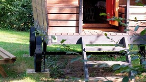 A wooden, covered structure with a door open, a bench outside, and a wheelbarrow nearby. - Camping de Thoissey - Val de Saône (Saint-Didier-sur-Chalaronne)