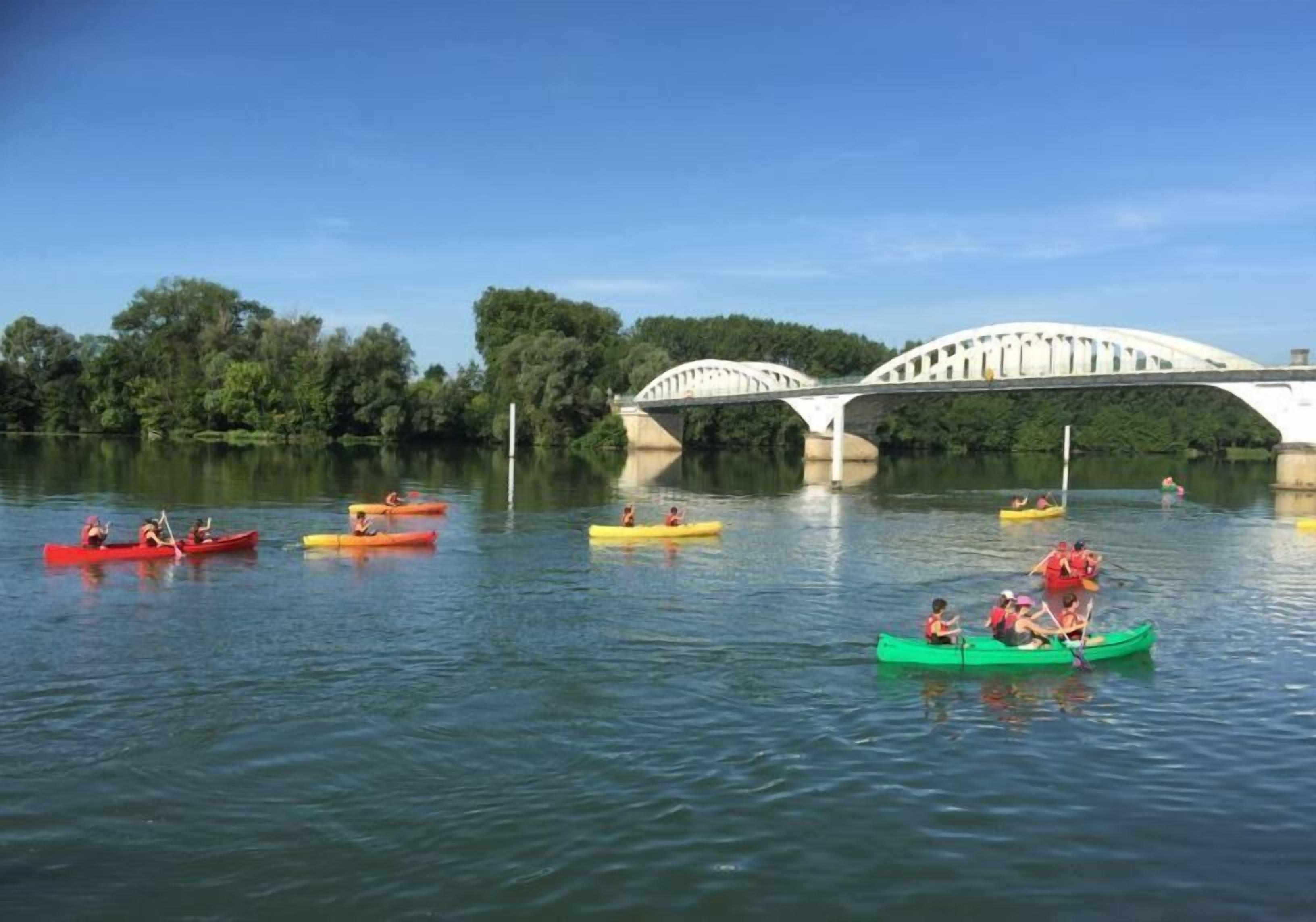 A group of people kayaking on a calm river with a bridge in the background.