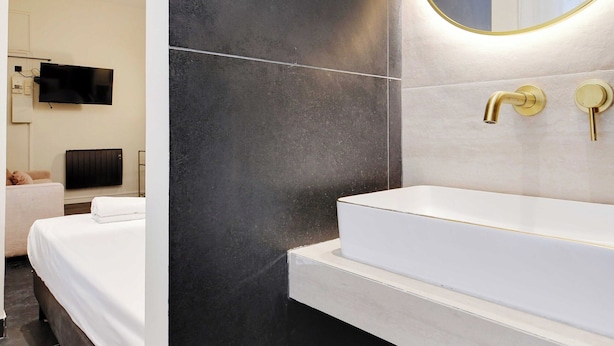 Un baño moderno con un espejo grande, un lavamanos blanco y una pared revestida de baldosas negras.