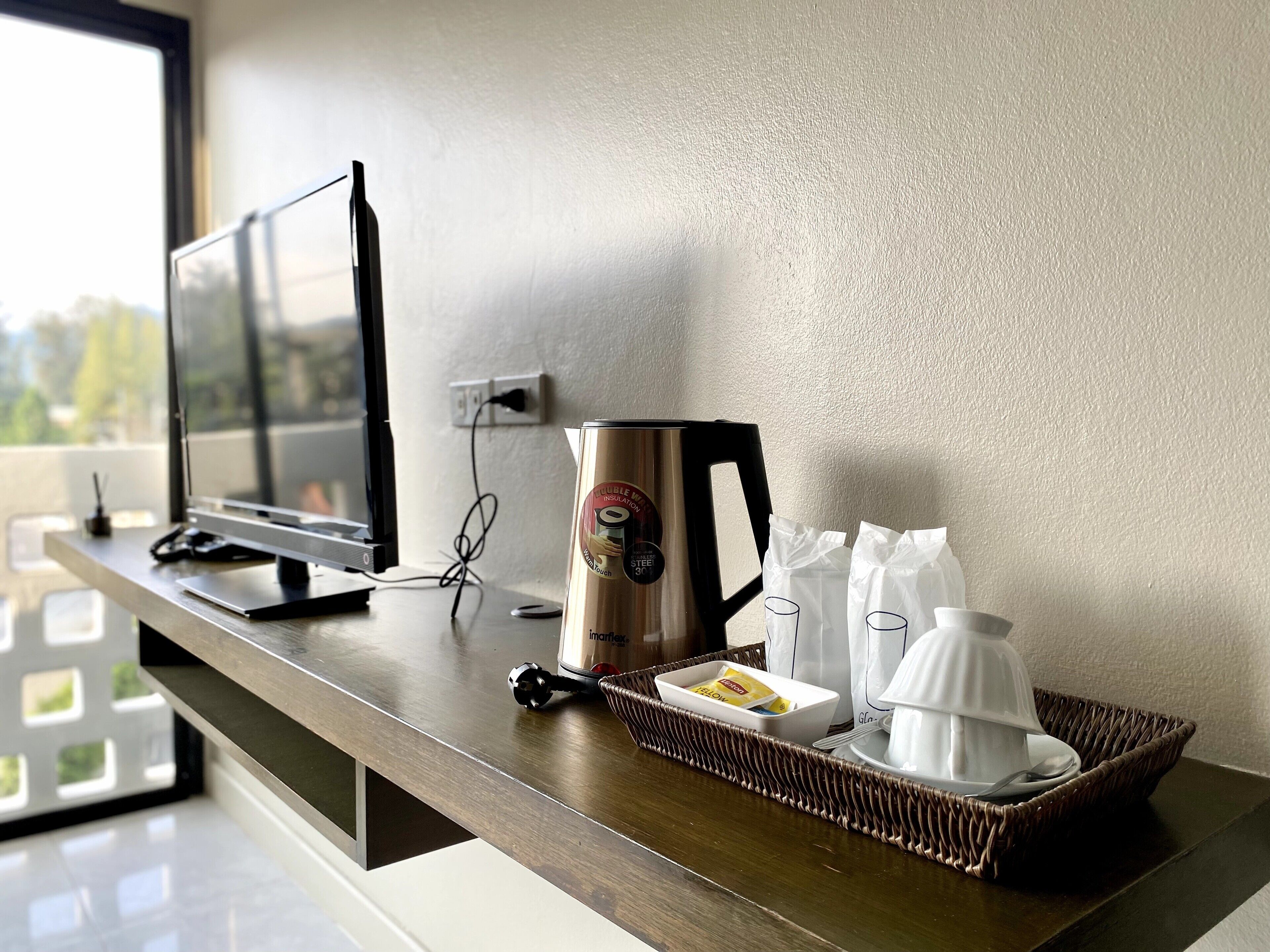 Quarto de hotel com escrivaninha, um computador, máquina de café, bandeja com caneca e garrafa de água.