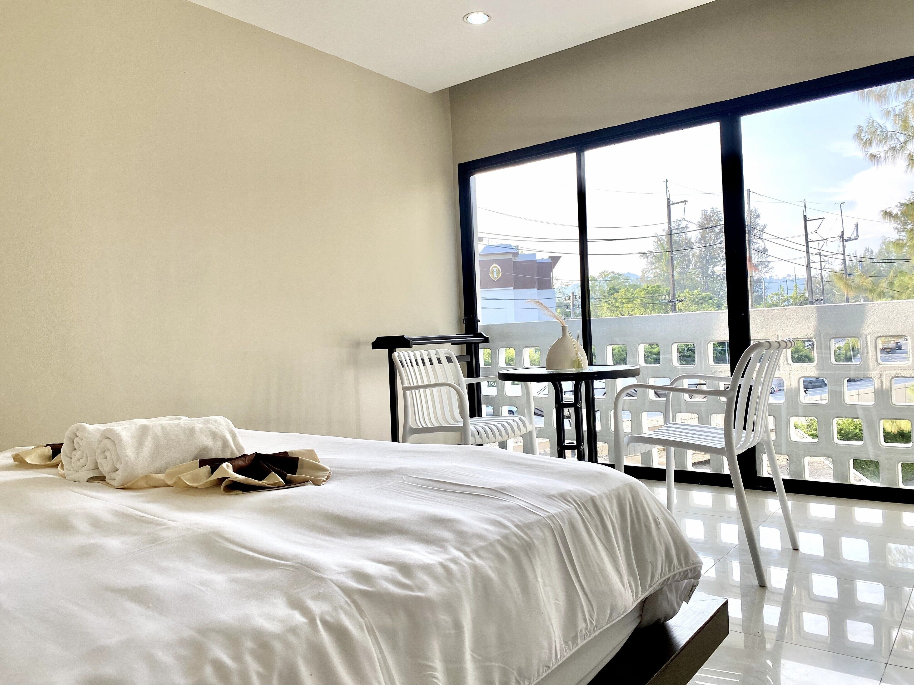 A hotel room with a bed, a small table, two chairs, and a balcony with a view of the outside.