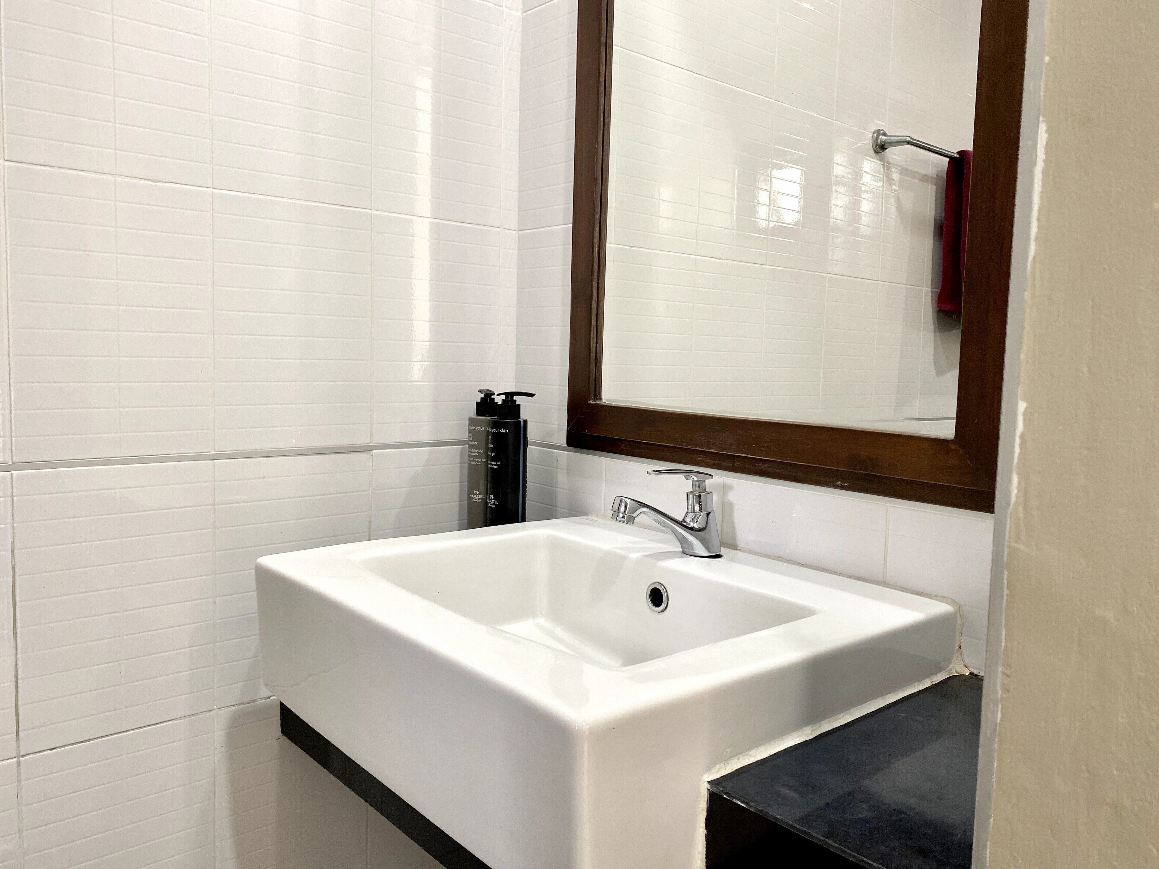 Um banheiro com paredes revestidas de azulejos brancos, uma pia branca com torneira cromada e um espelho com moldura de madeira.