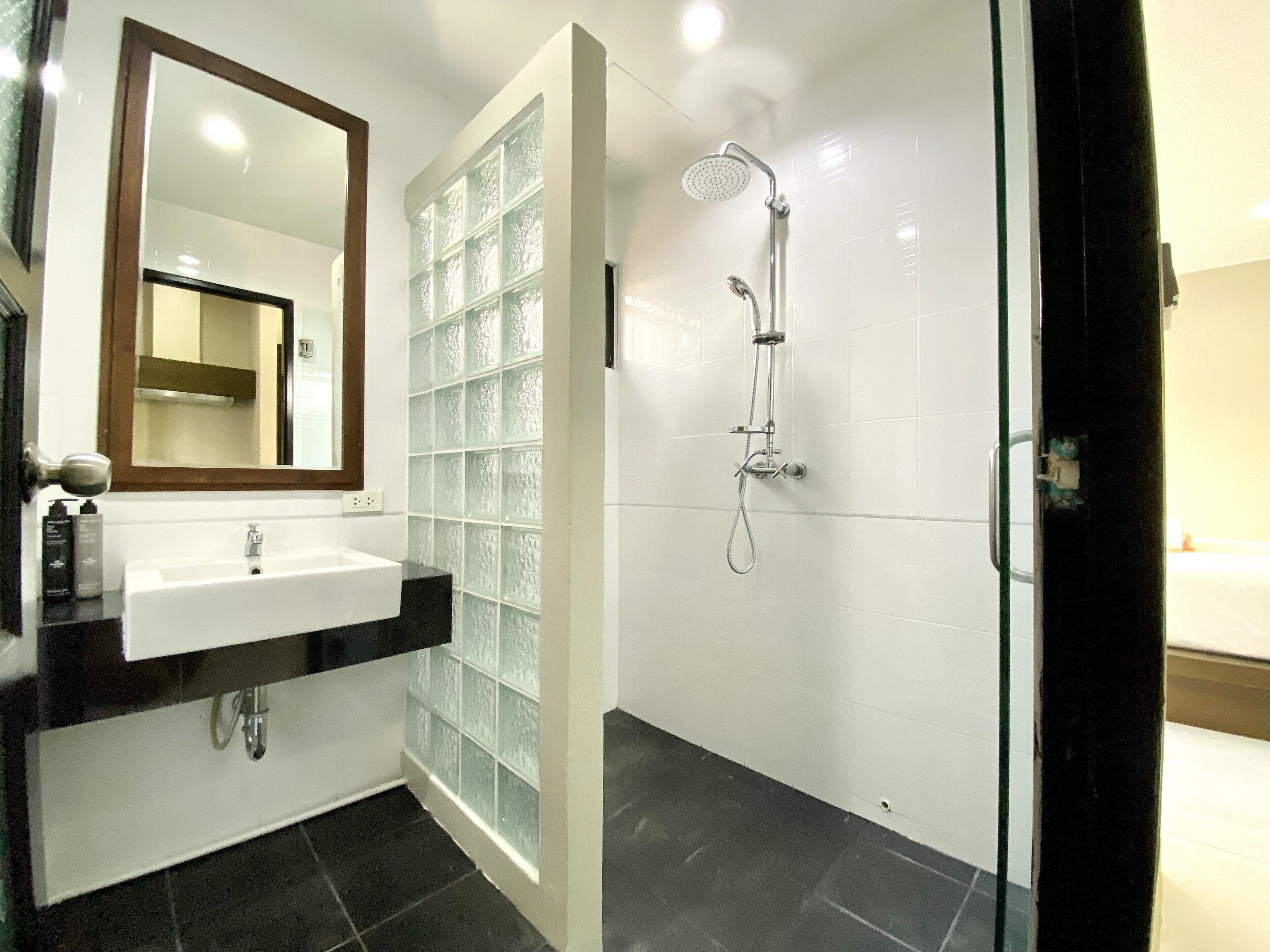 Een moderne badkamer met een glazen douchecabine, een witte wastafel en een spiegel met houten lijst.