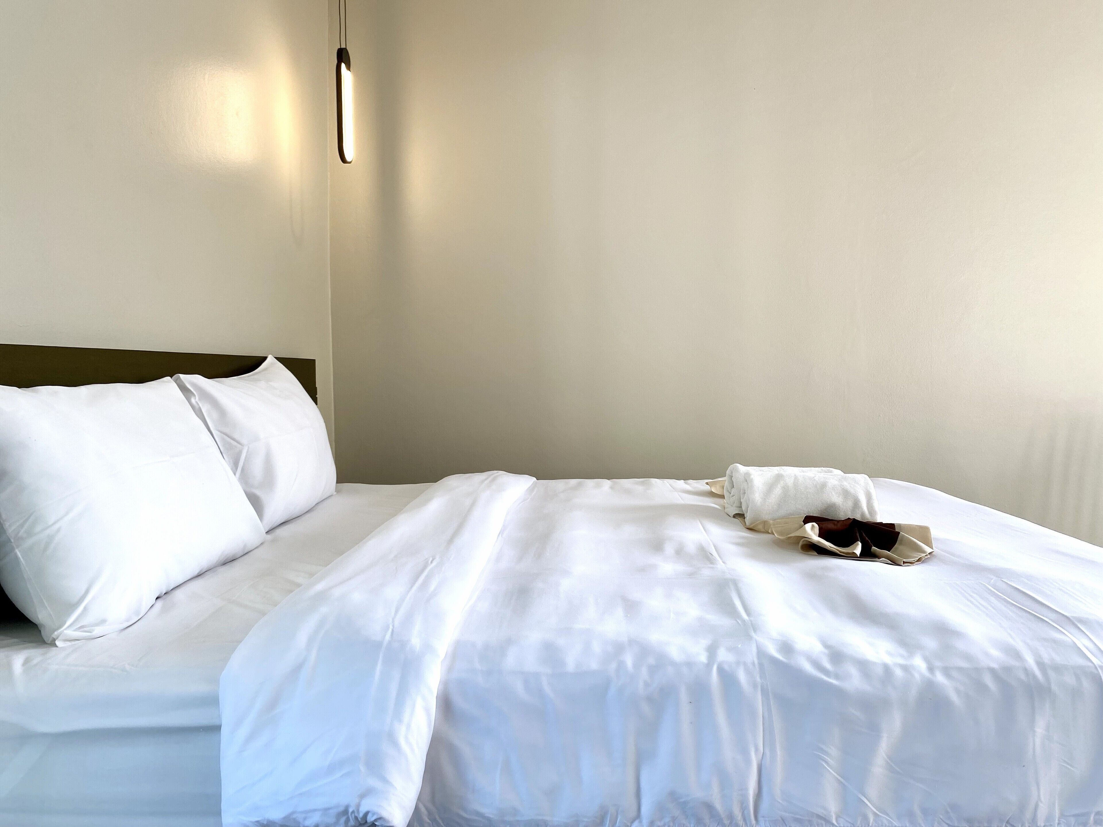 A neatly made bed with white linens, a headboard, and a bedside lamp.