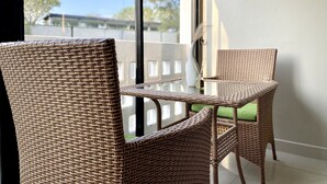 Ein Korbsessel-Set mit Tisch neben einem Fenster mit Blick auf Bäume und ein Gebäude.