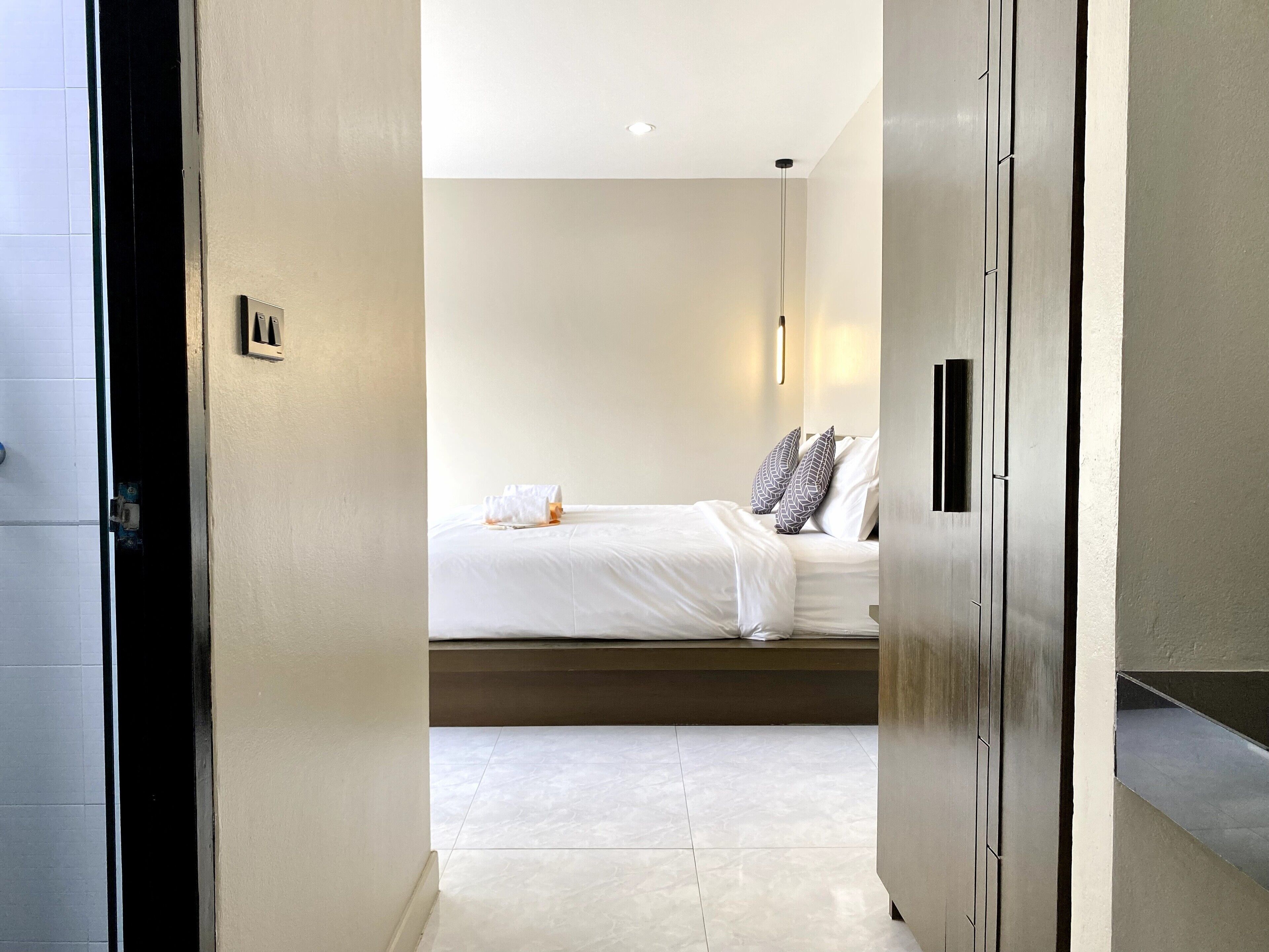 A modern hotel room with a bed, white linens, and a bedside table.