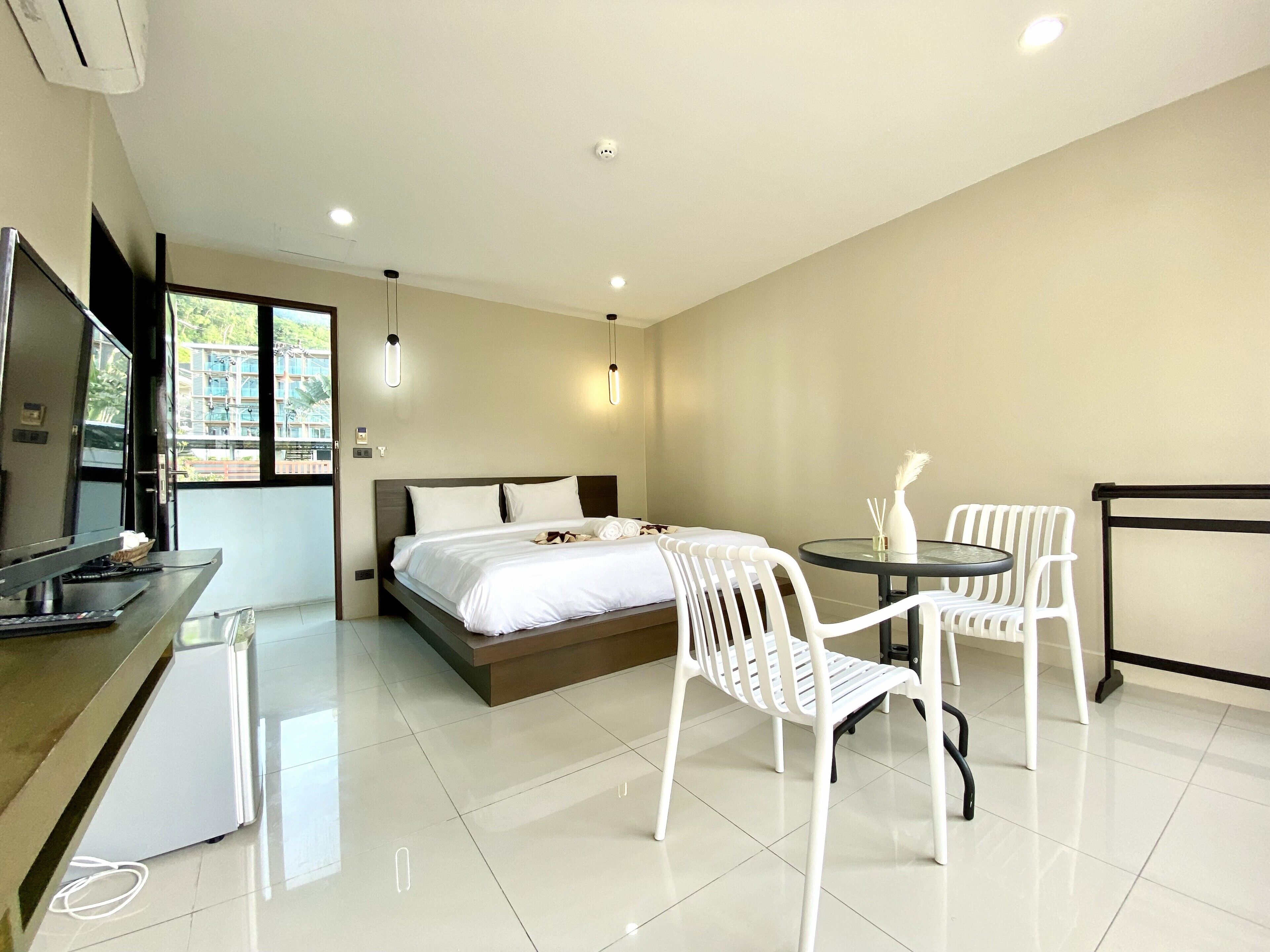 A hotel room with a bed, a desk with a TV, and two white chairs around a small table.