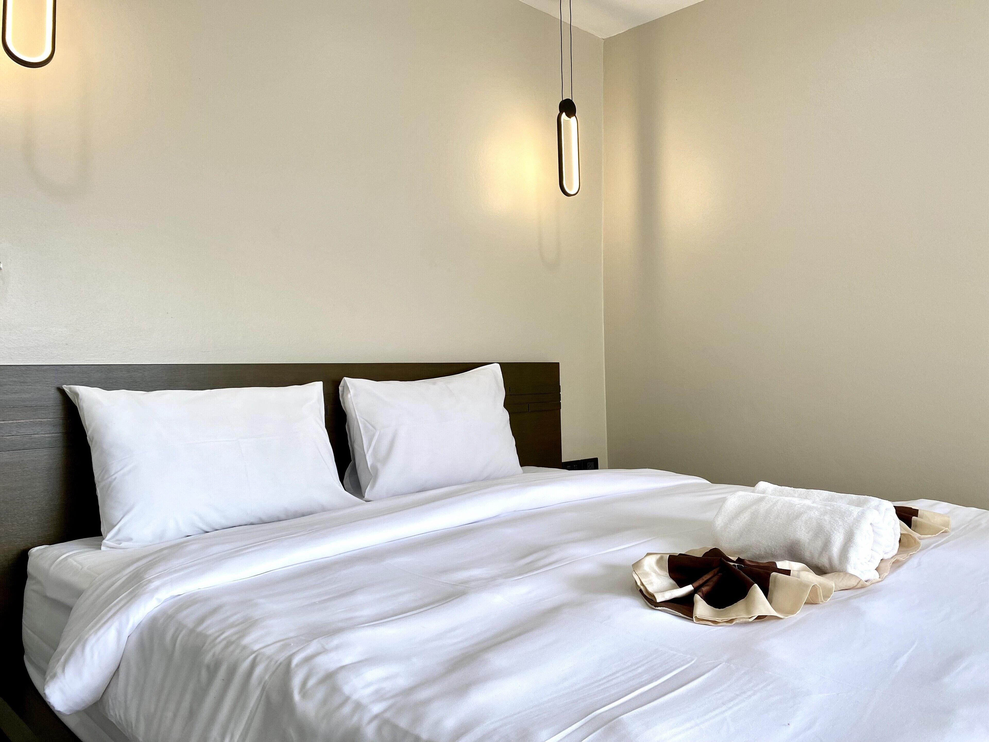 A neatly made bed with white linens and pillows, a wooden headboard, and a hanging light fixture.